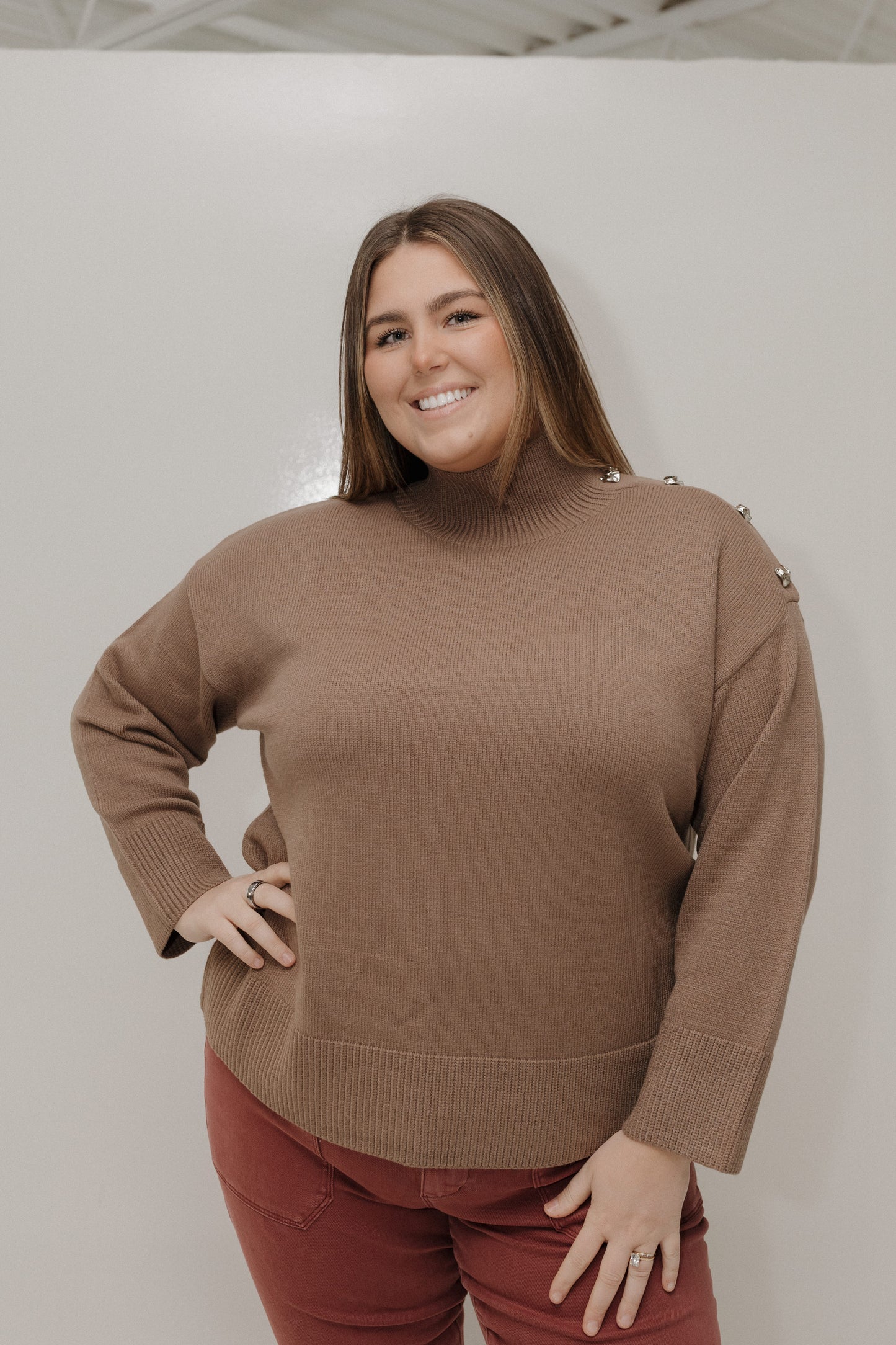 Woman wearing a brown sweater and red pants against a plain background