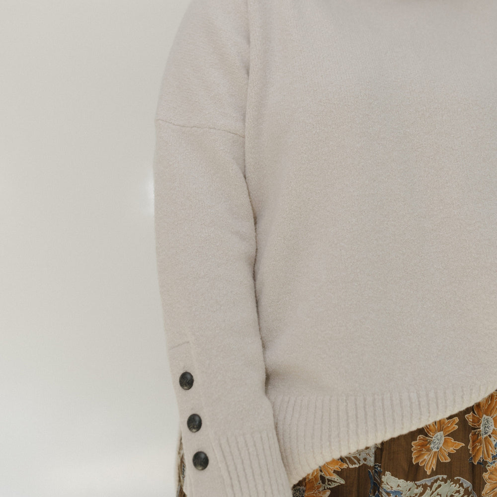 Person wearing a beige sweater with button details on a plain background