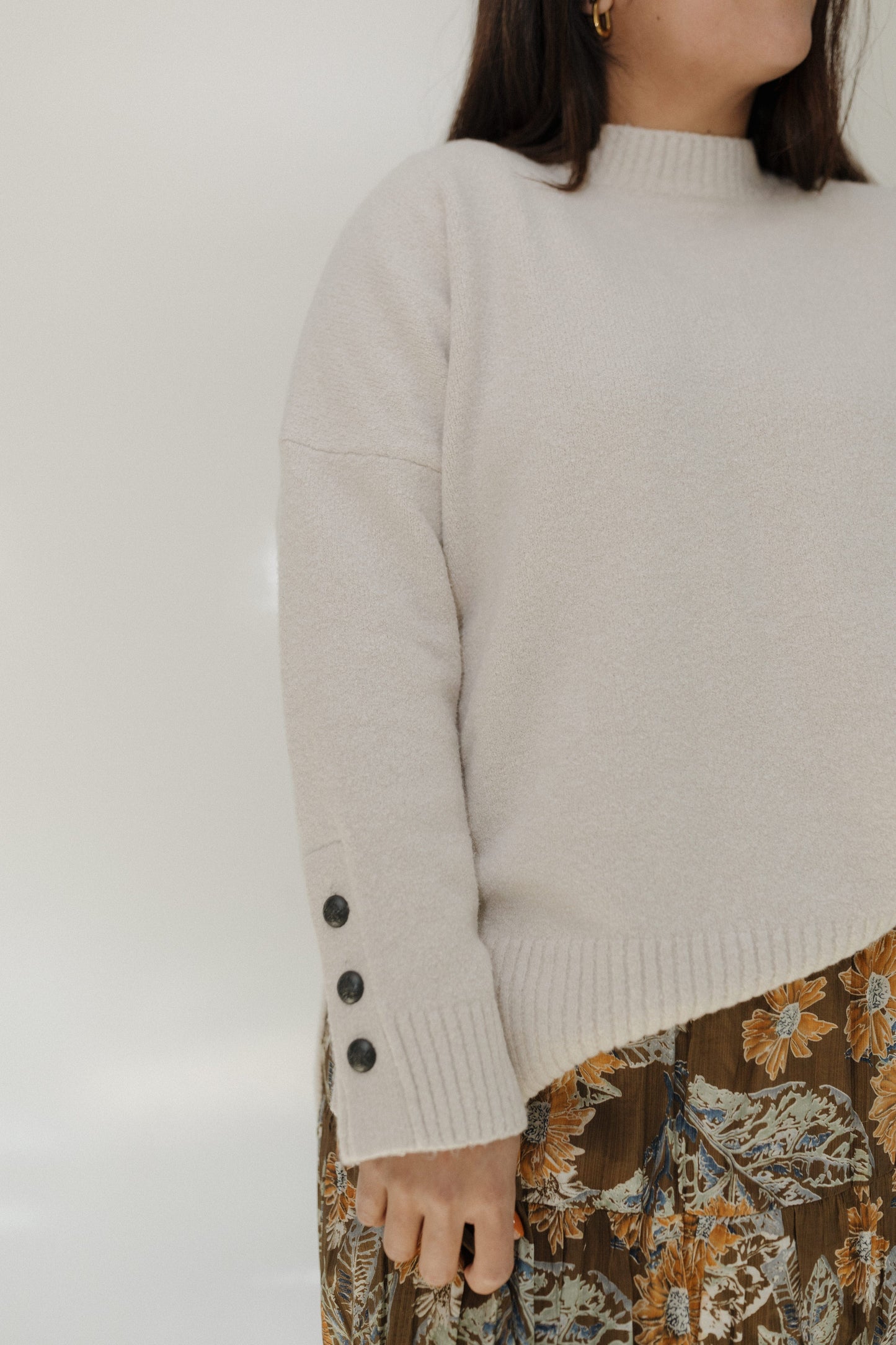 Person wearing a beige sweater with button details on a plain background