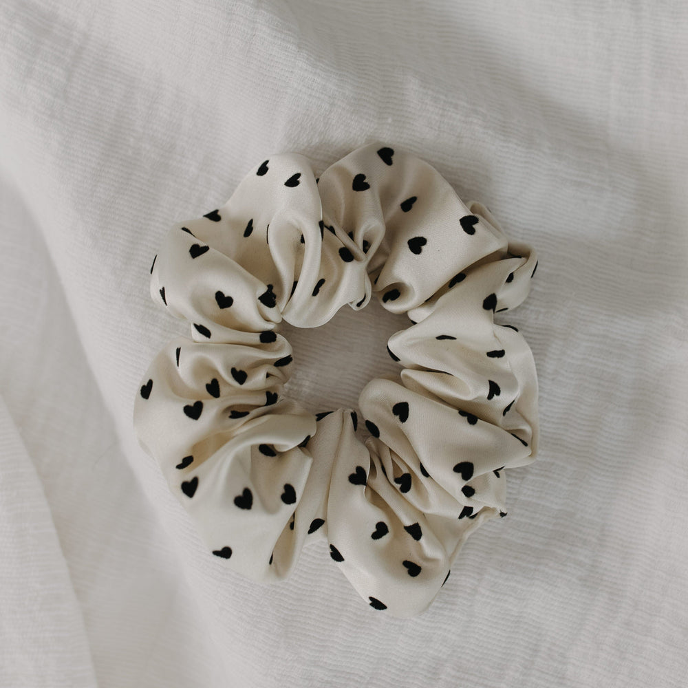White scrunchie with black heart patterns on a white fabric background