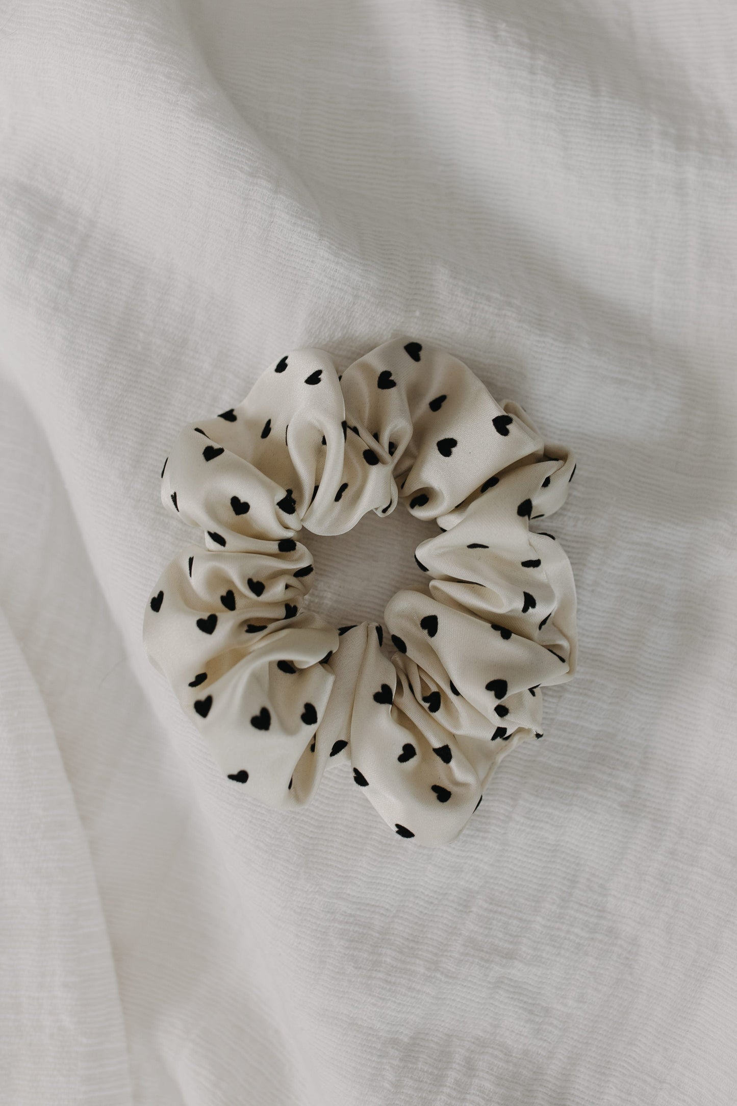 White scrunchie with black heart patterns on a white fabric background