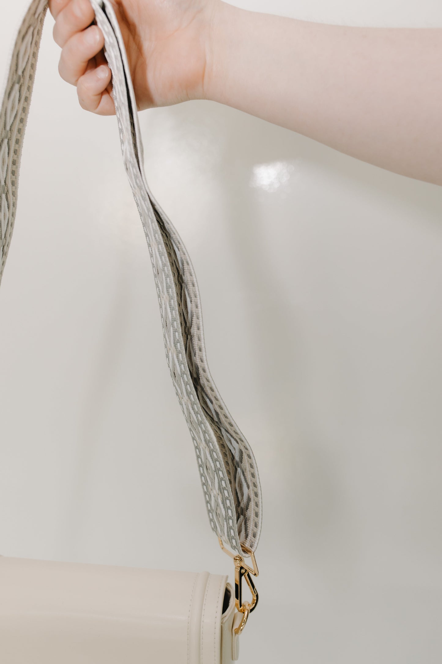 Close-up of a hand holding handbag's guitar strap with a neutral background