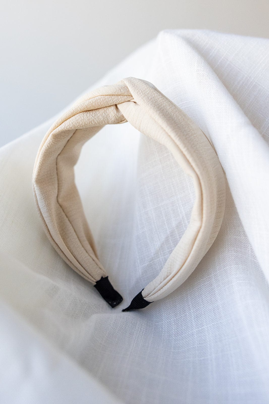 The CRINKLE TEXTURE HEADBAND WITH KNOT IN SAND by Love Marlow is elegantly displayed on a white textured surface.