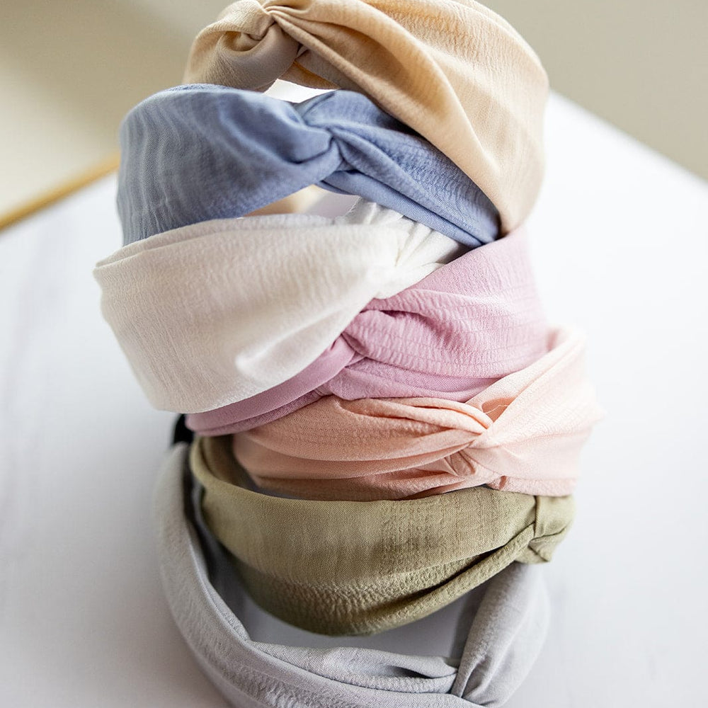 A stack of colorful headbands, featuring a twisted knot design and crinkle texture, sits gracefully on a white surface. The hues—beige, blue, pink, and green—mirror the enchanting twilight sky.