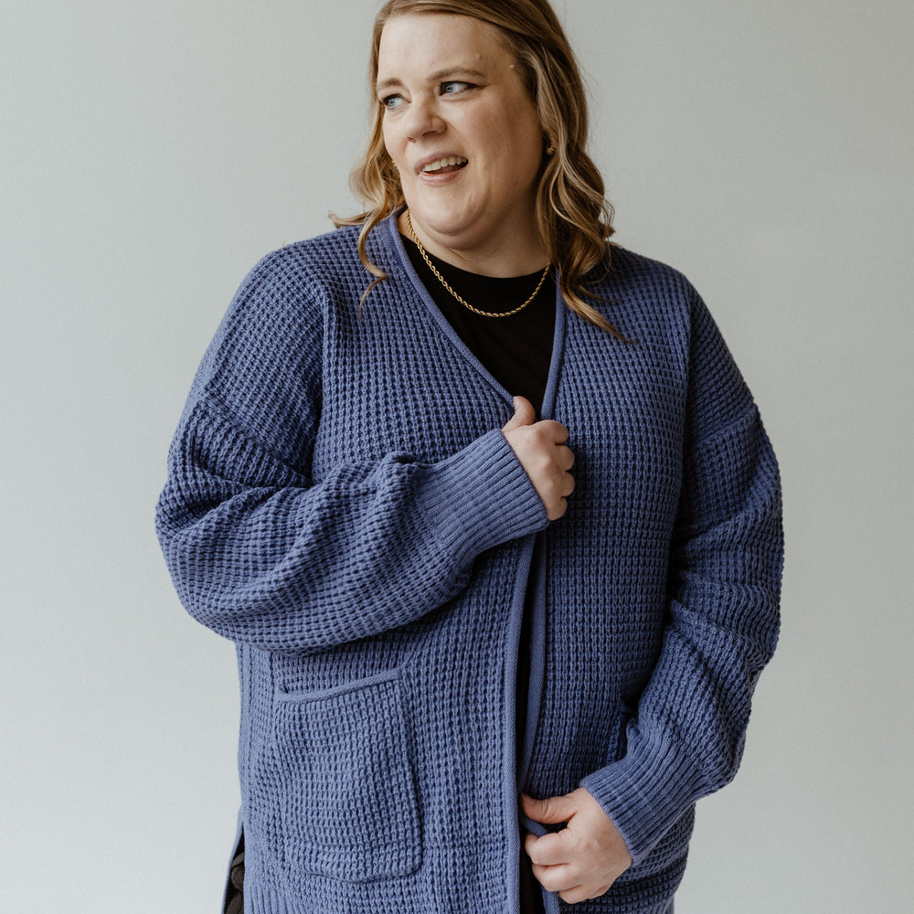 A person wearing a French Blue crochet knit cardigan over a black shirt stands against a plain background.