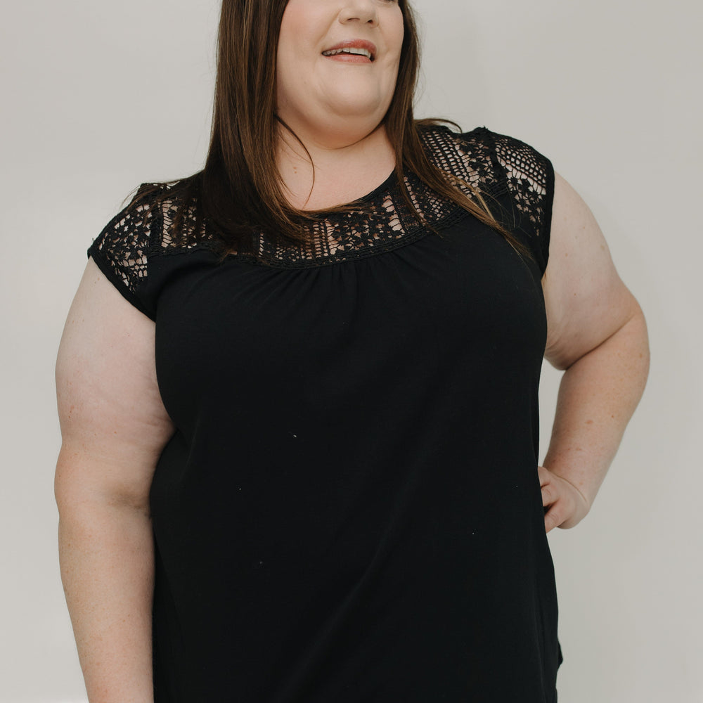 Woman wearing a black top with lace details on a plain background