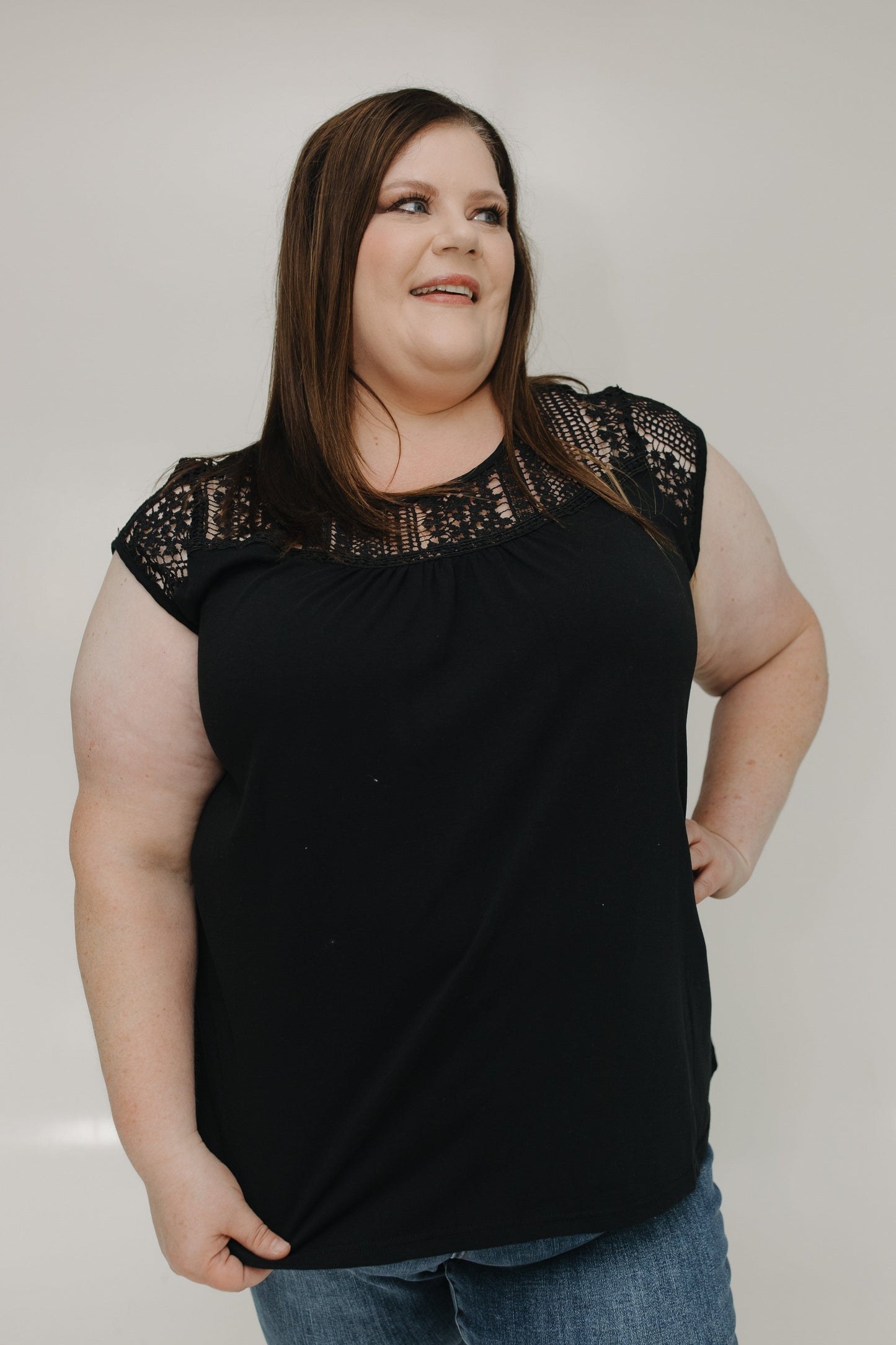 Woman wearing a black top with lace details on a plain background