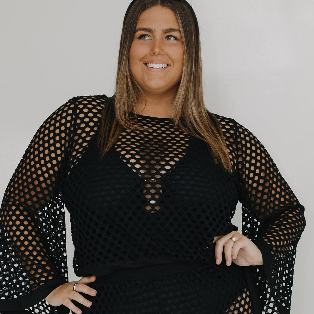 Woman wearing a black fishnet outfit against a plain background