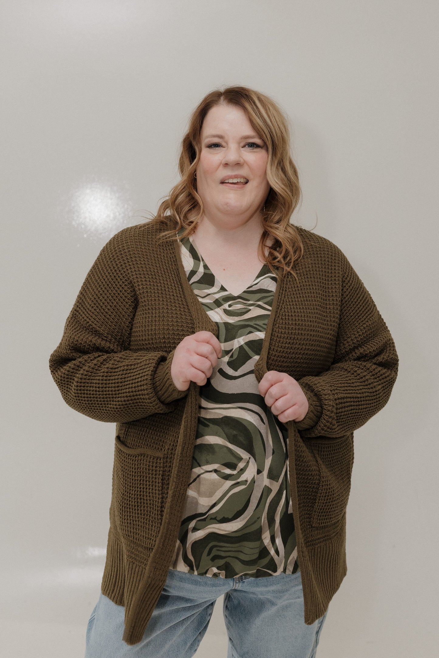 Woman wearing a brown cardigan over a patterned top with a plain background
