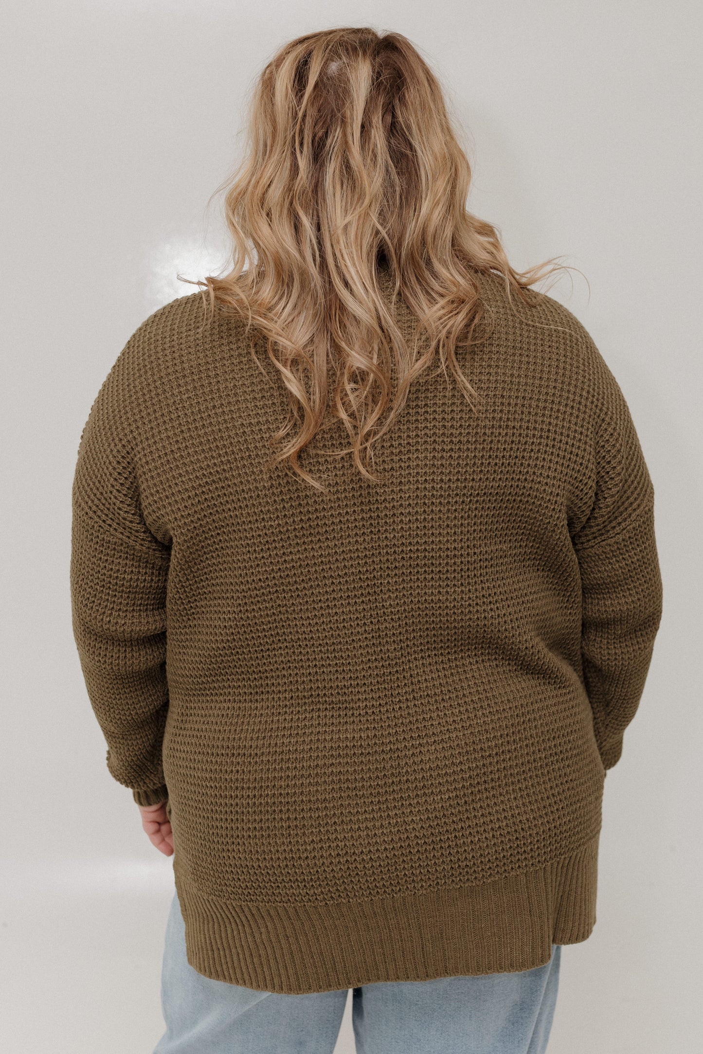 Person wearing a brown knitted cardigan on a plain background
