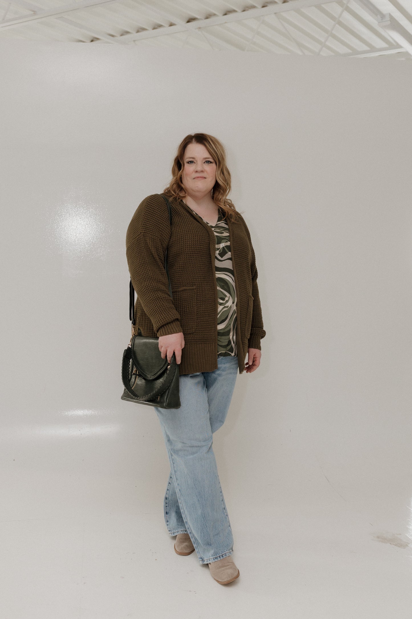 Woman wearing a brown cardigan, patterned top, and jeans in a white studio setting