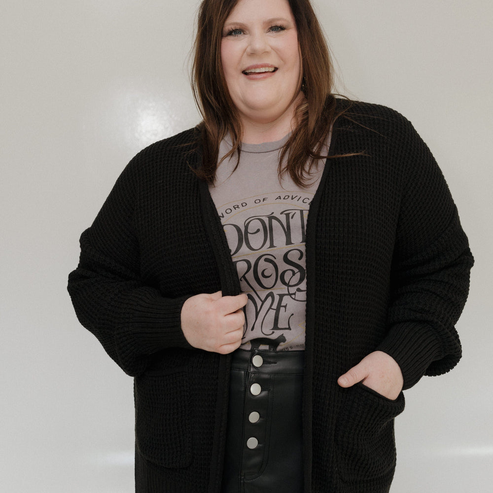 Person wearing a black cardigan over a graphic t-shirt with text, standing against a plain background.