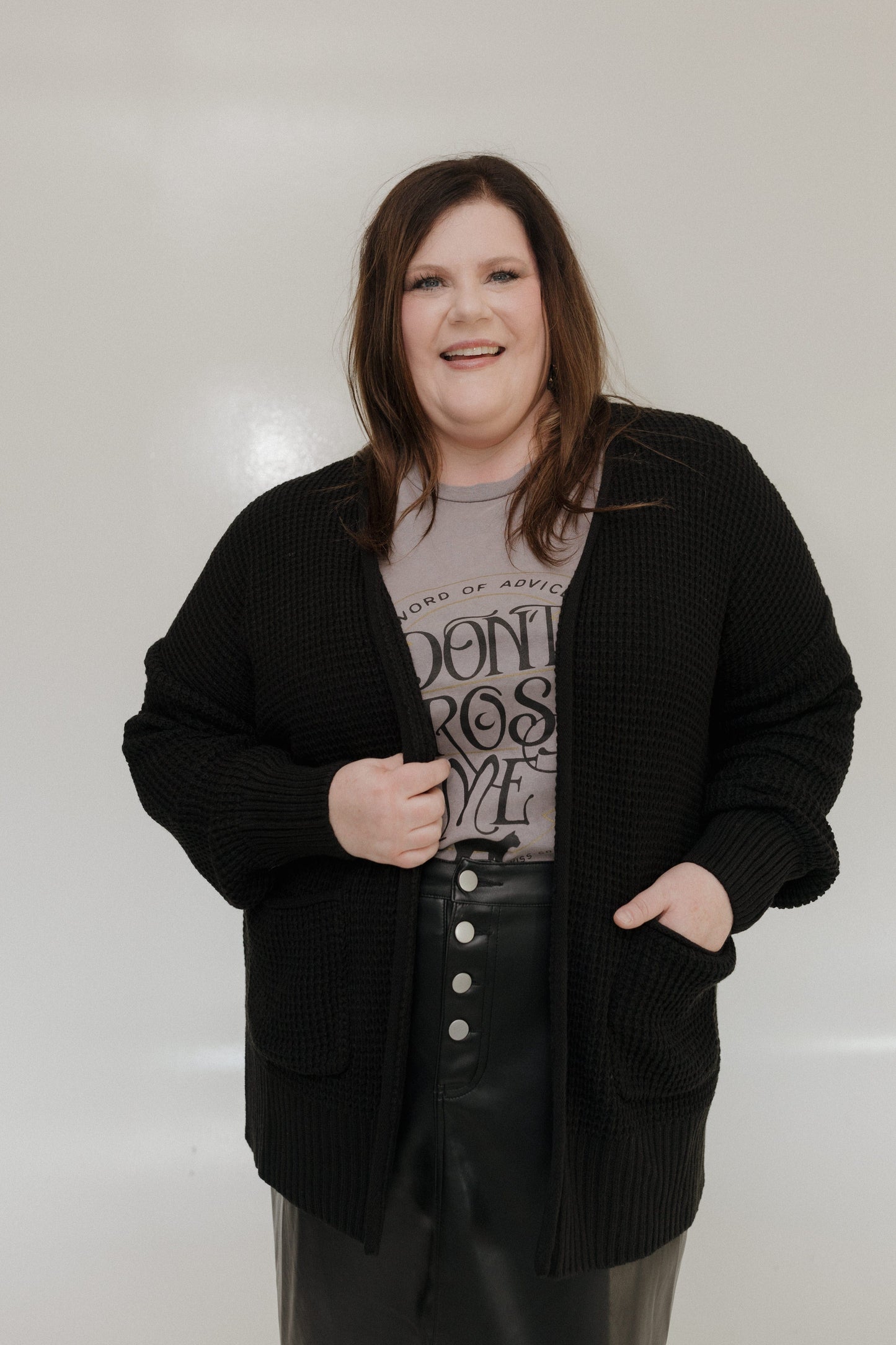 Person wearing a black cardigan over a graphic t-shirt with text, standing against a plain background.