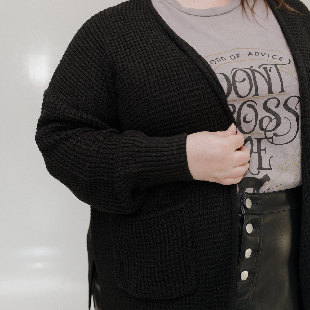 Person wearing a black cardigan over a graphic t-shirt with text.