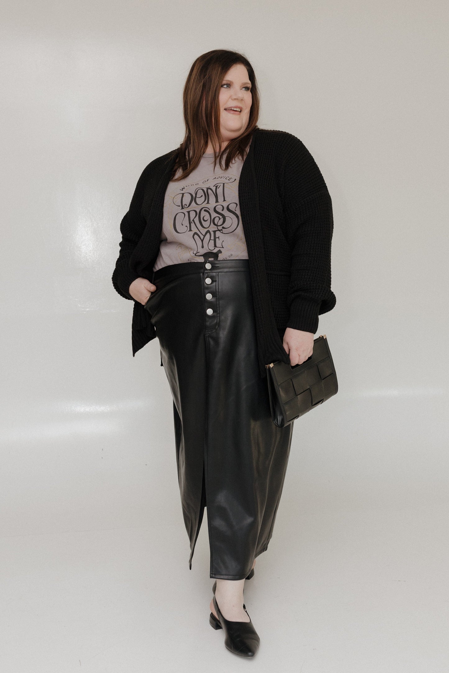 Person wearing a black cardigan, graphic t-shirt, and leather pants on a white background