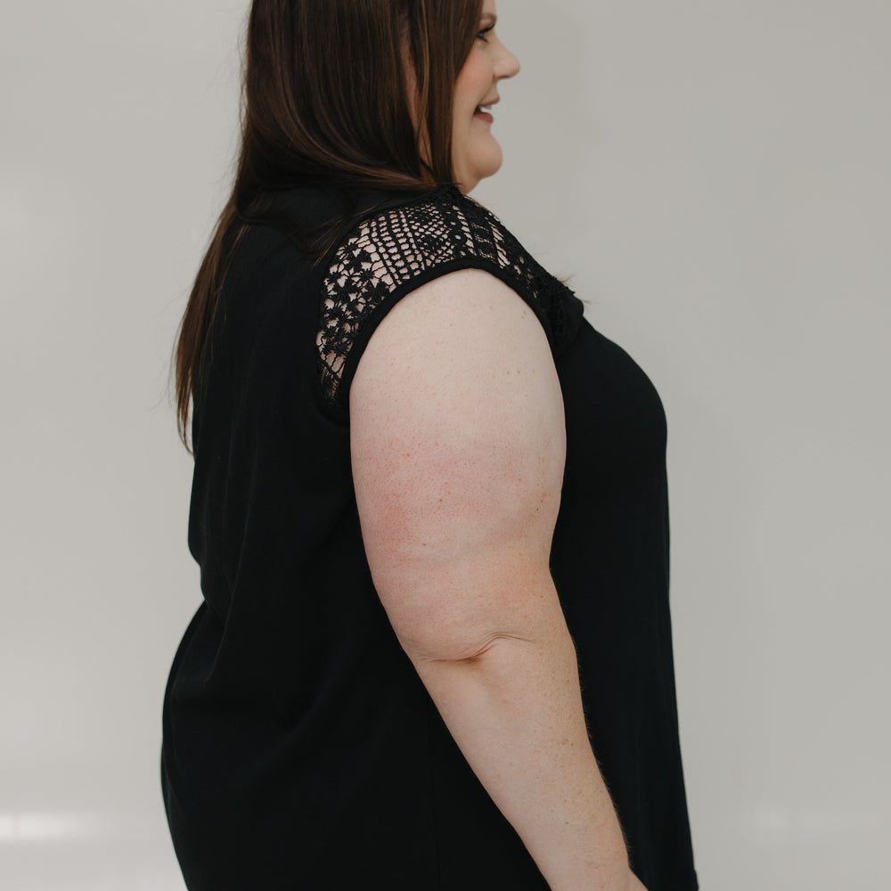 Woman wearing a black sleeveless top with embellishments on a plain background