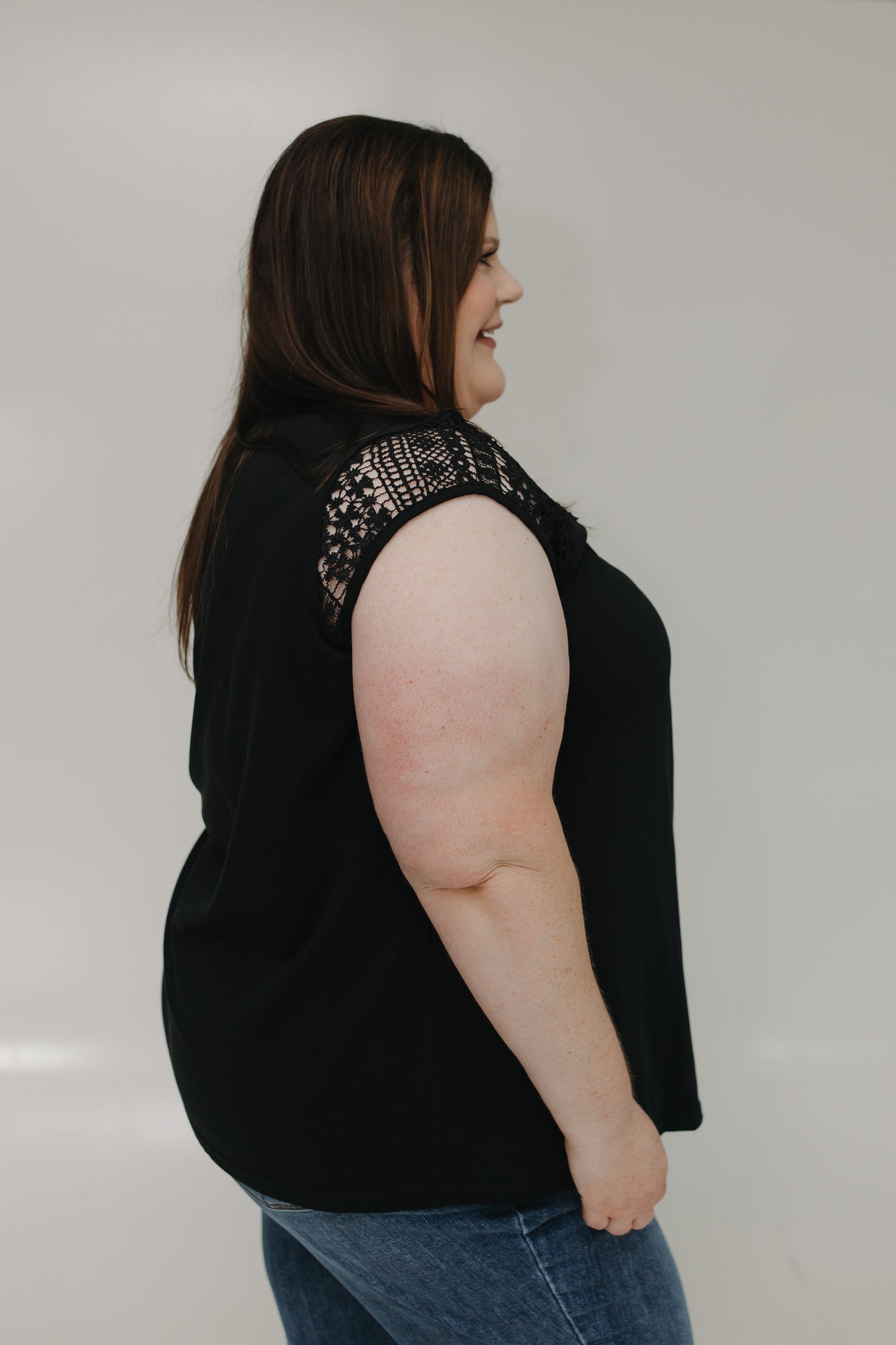 Woman wearing a black sleeveless top with embellishments on a plain background