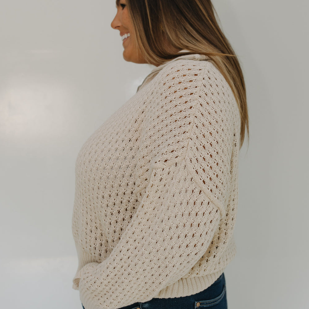 Woman wearing a beige chunky knit sweater and blue jeans against a plain background