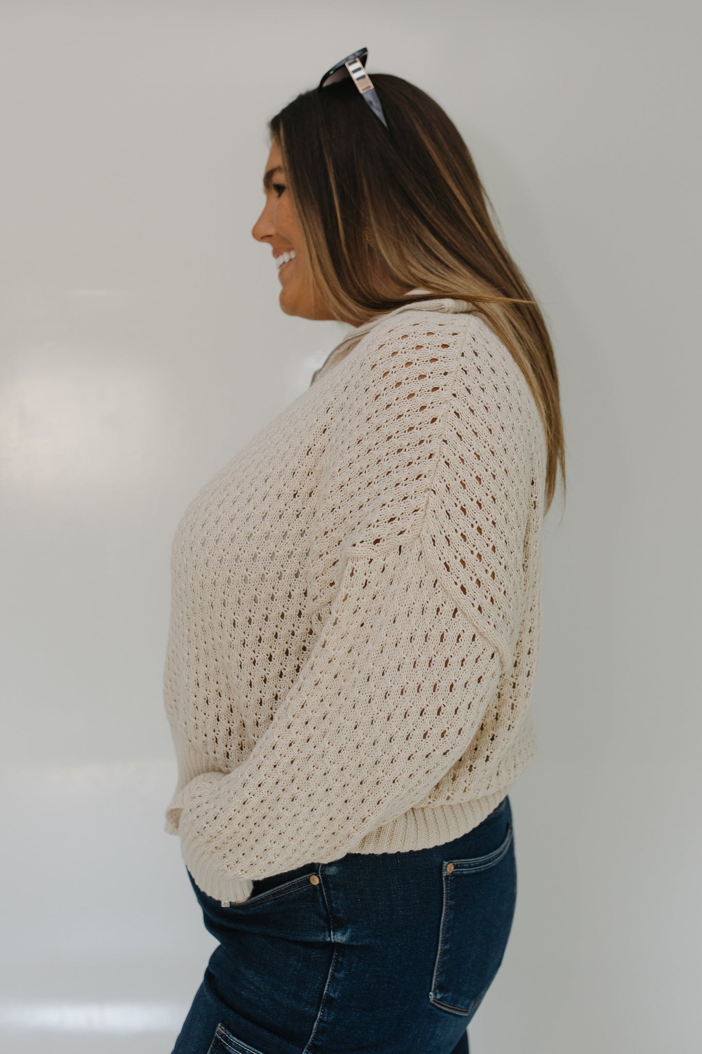 Woman wearing a beige chunky knit sweater and blue jeans against a plain background