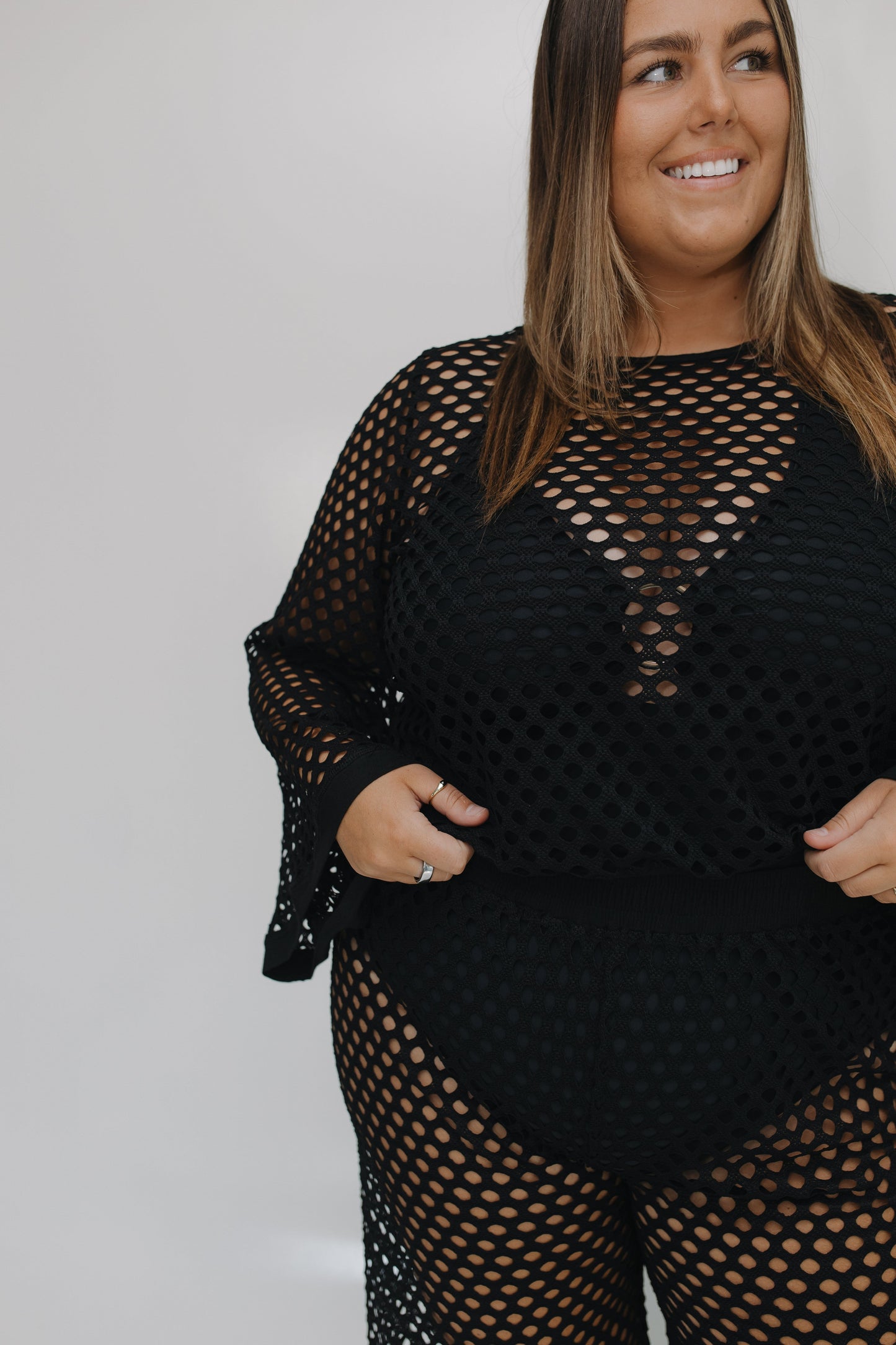 Woman wearing a black fishnet outfit against a plain background