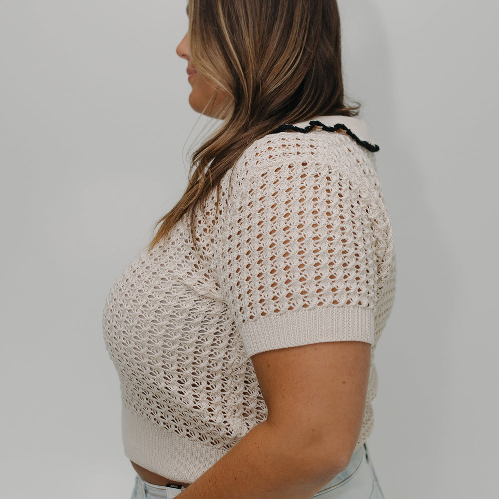 Woman wearing a beige knitted top and light blue jeans against a white background