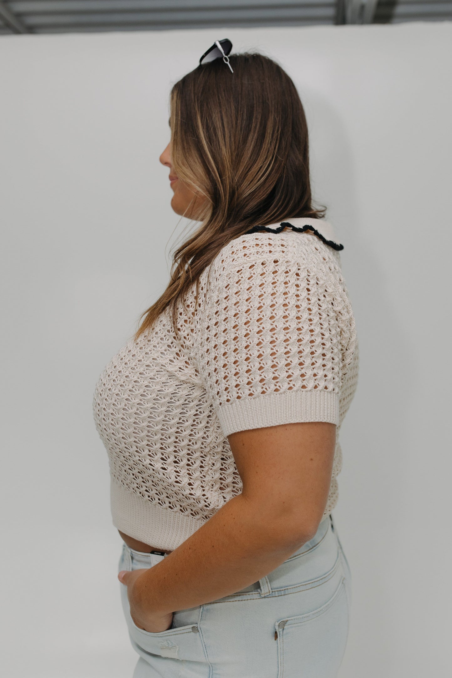 Woman wearing a beige knitted top and light blue jeans against a white background