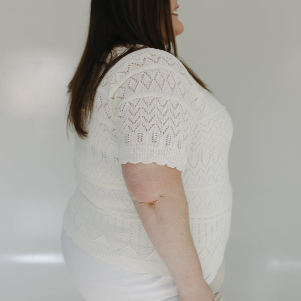 Woman wearing a white knit sweater against a plain background