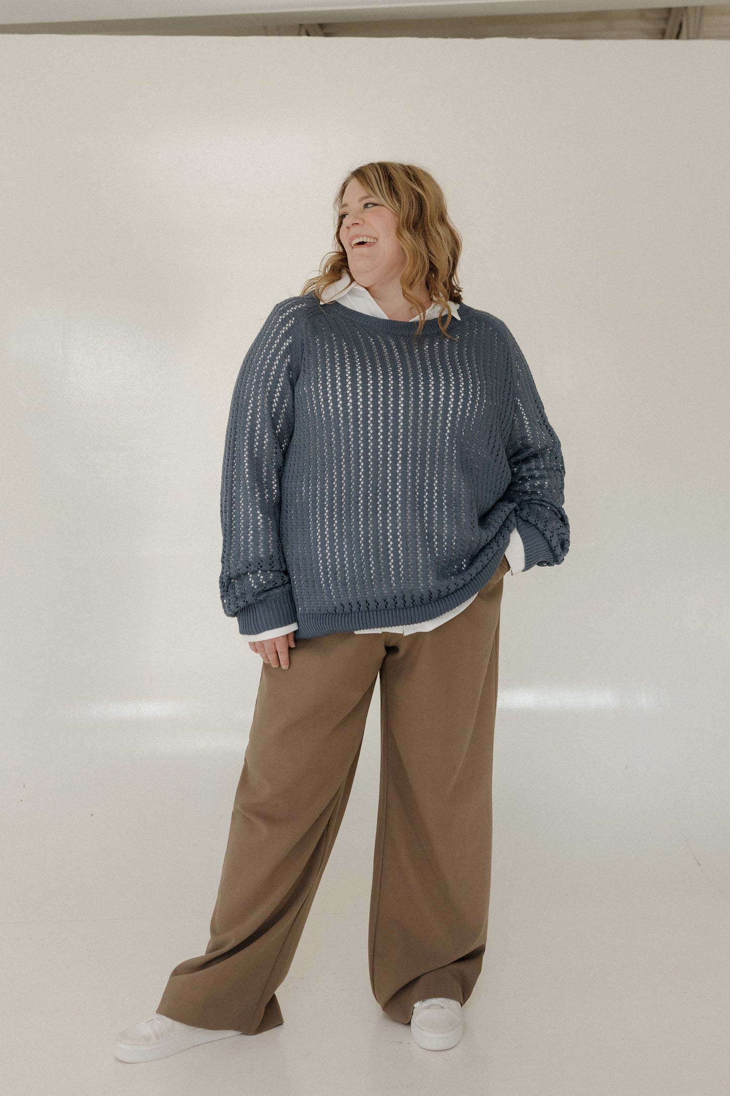 Person wearing a blue knitted sweater and brown pants on a white background