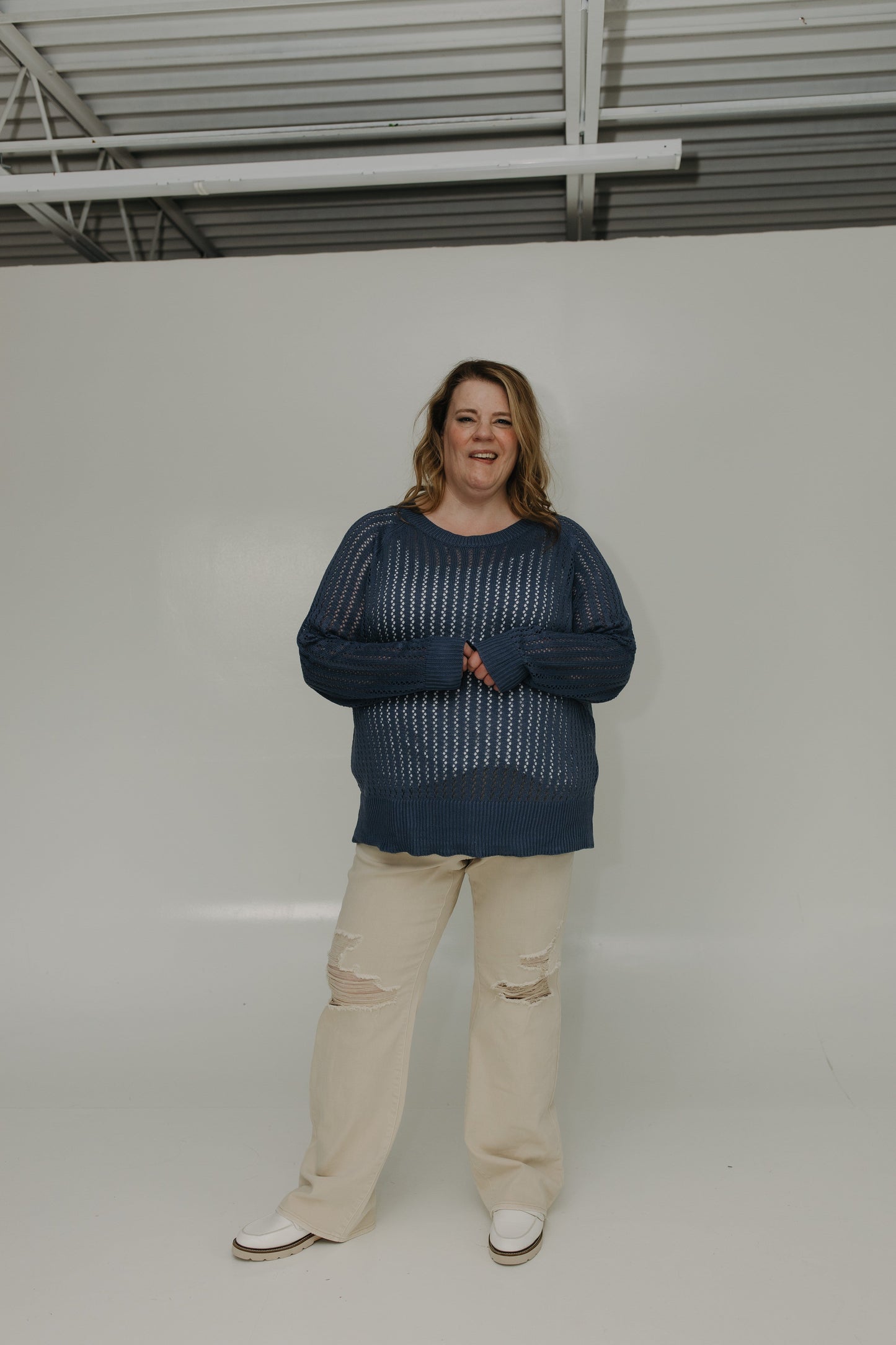 Person wearing a blue sweater and beige pants standing against a white background