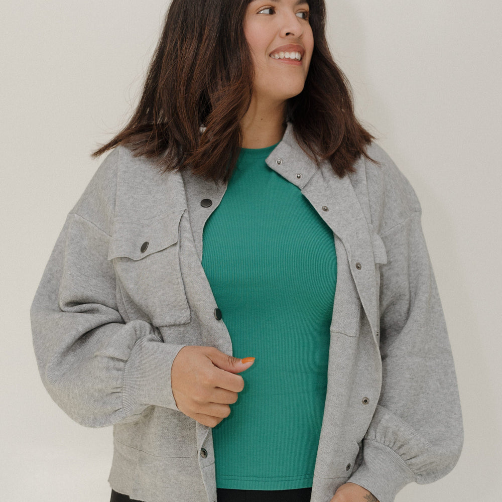 Woman wearing a gray jacket over a green shirt with a plain background