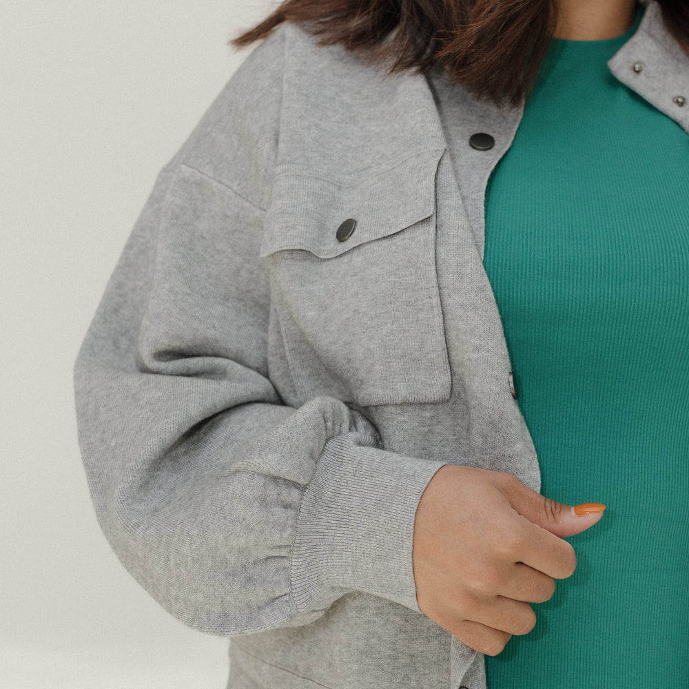 Person wearing a gray jacket over a green top on a plain background