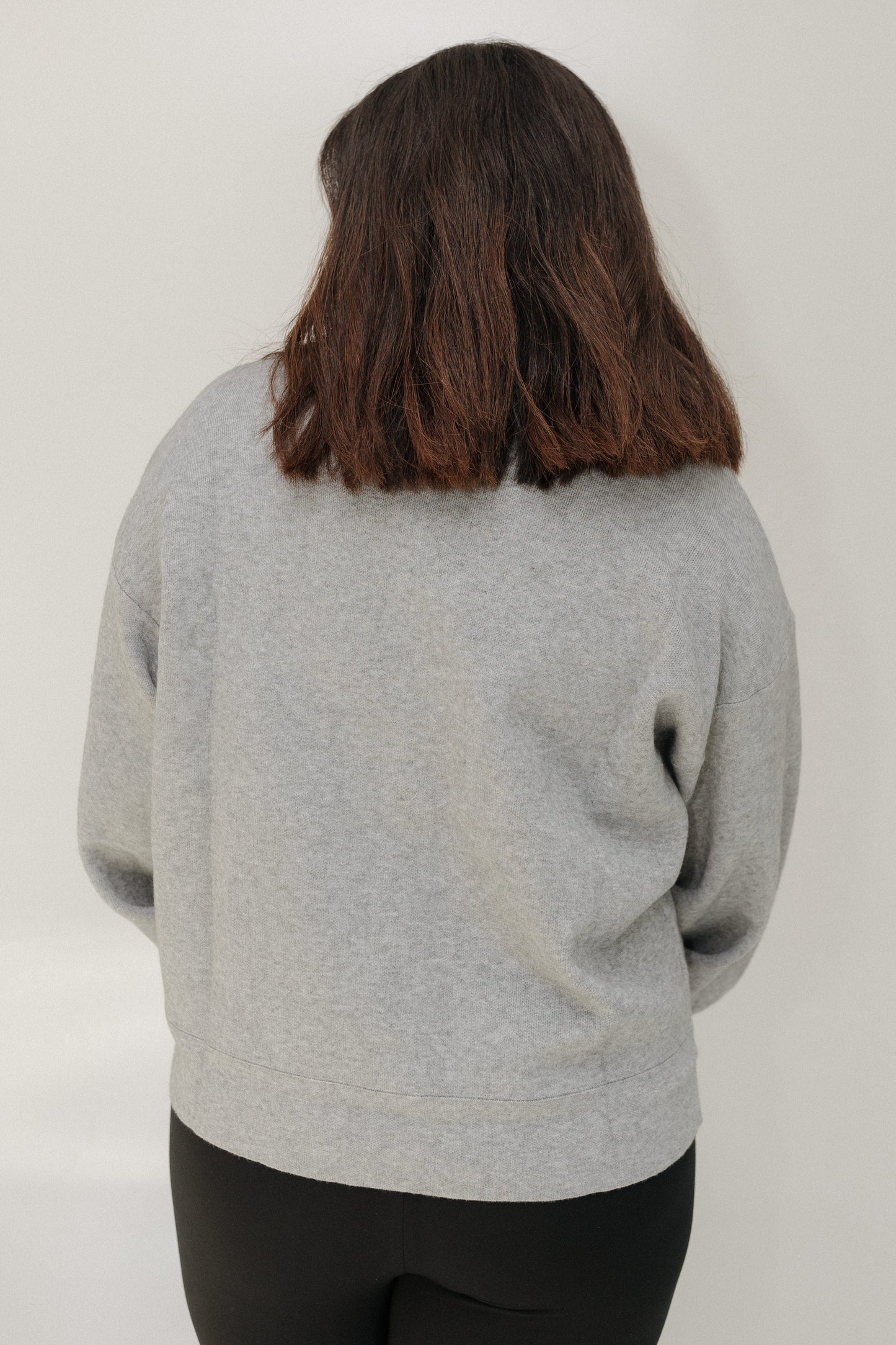 Person wearing a gray sweater from behind on a plain background