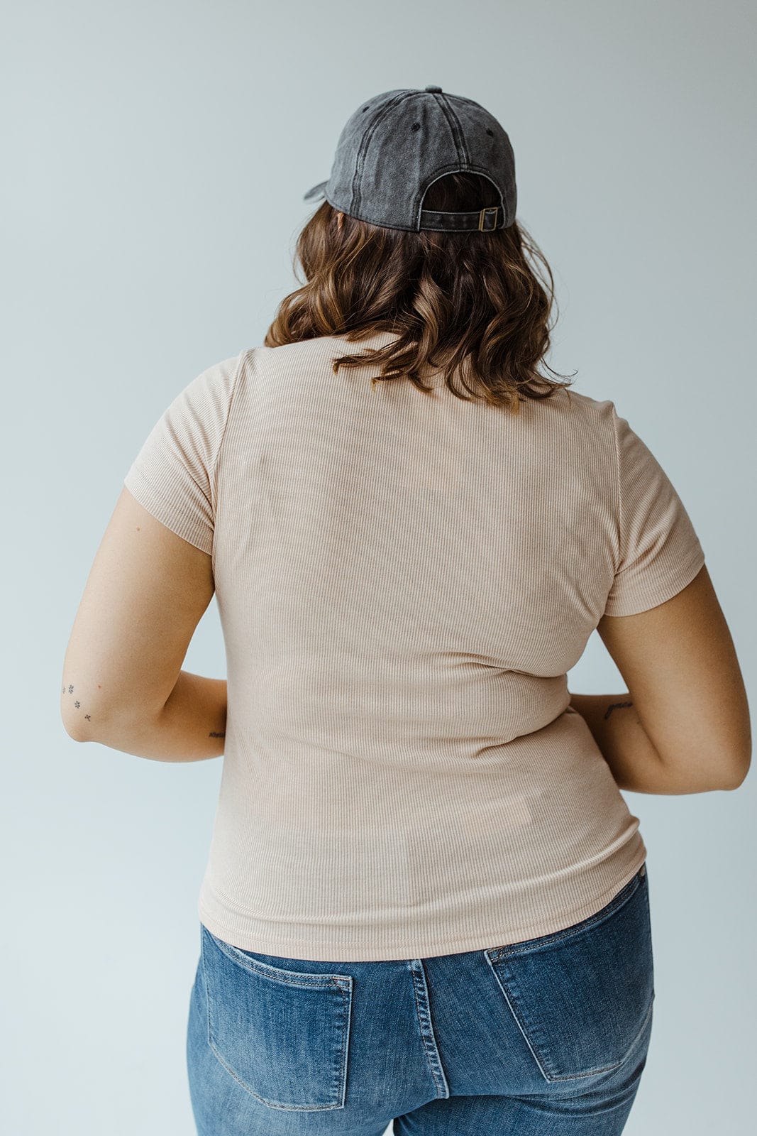 Person wearing a lightweight, cozy fit beige shirt, blue jeans, and a gray cap, facing away.