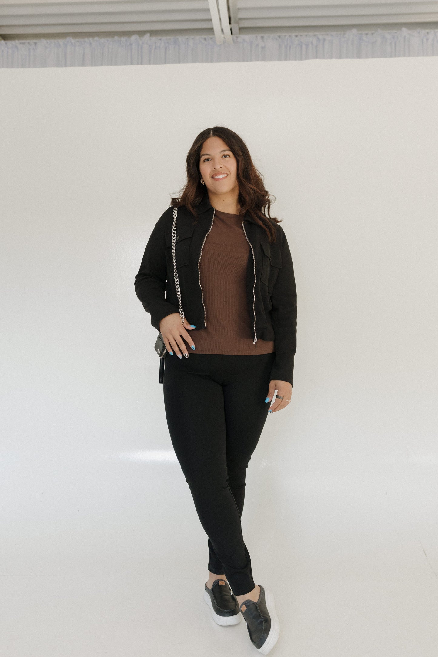 Woman wearing a black jacket and pants standing against a white wall