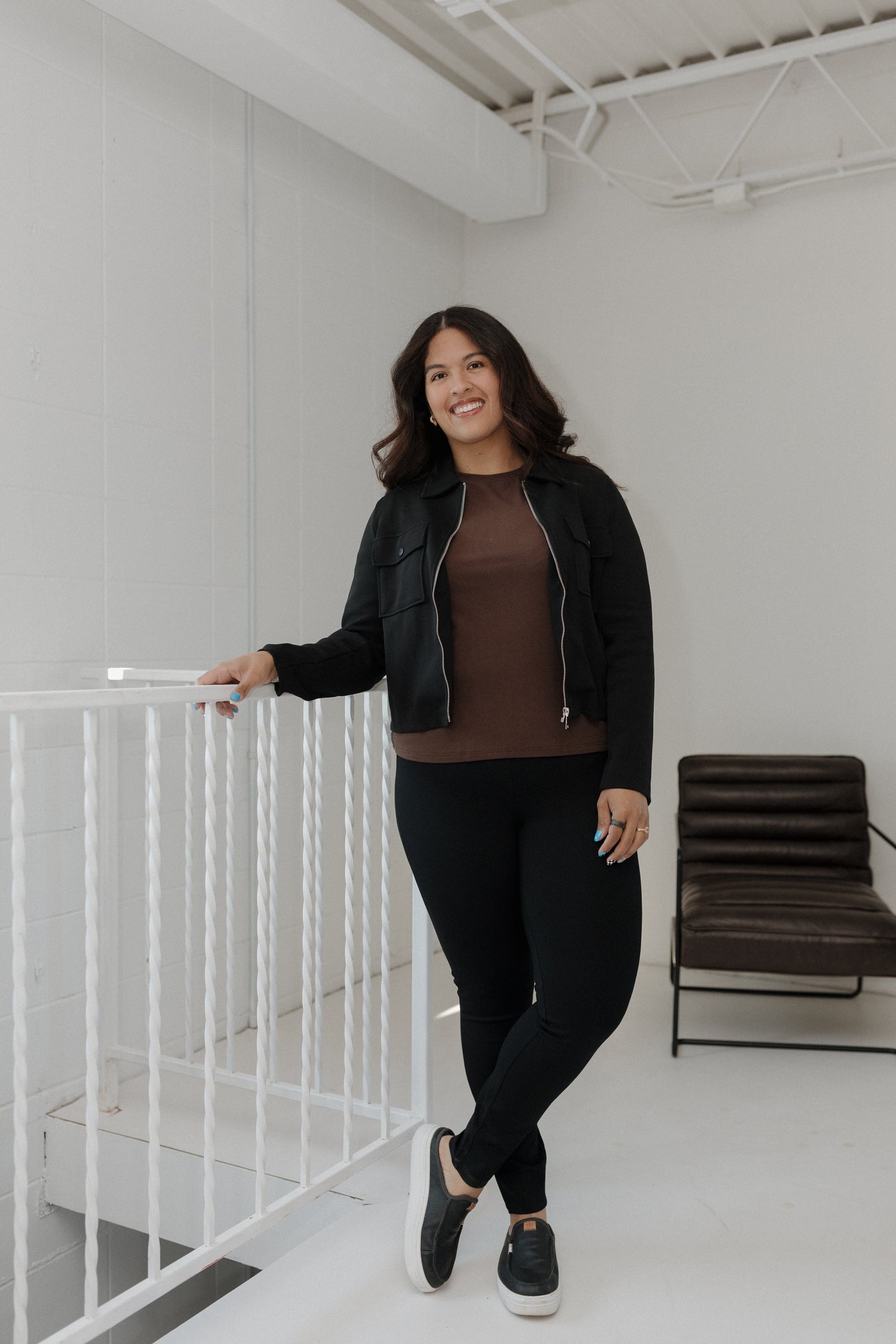 Woman standing in a minimalistic room with white walls and a black chair.