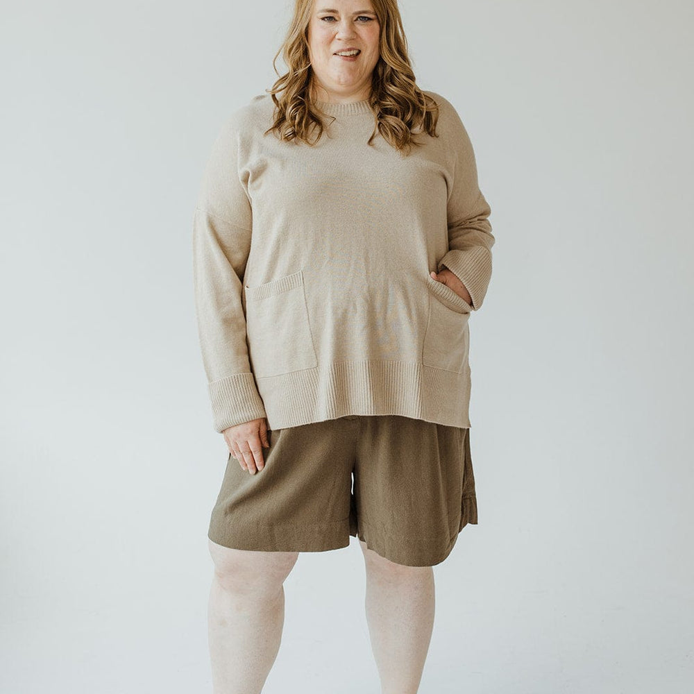 A woman wearing Yesta's classic beige Cuffed Sweater with Pockets, paired with olive green shorts and beige slip-on shoes, stands against a plain background.