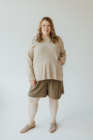 A woman wearing Yesta's classic beige Cuffed Sweater with Pockets, paired with olive green shorts and beige slip-on shoes, stands against a plain background.