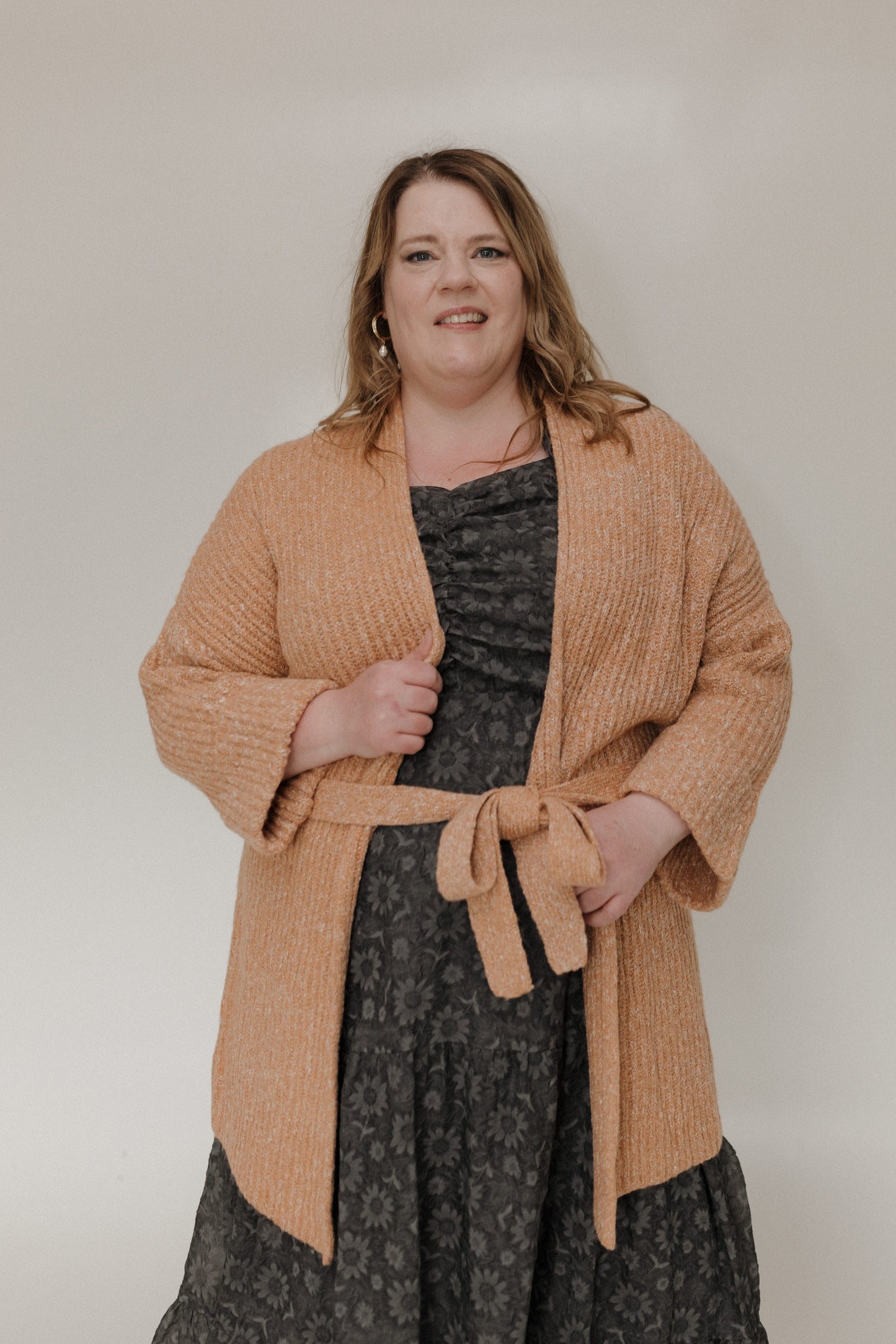 Woman wearing a beige cardigan over a patterned dress against a plain background