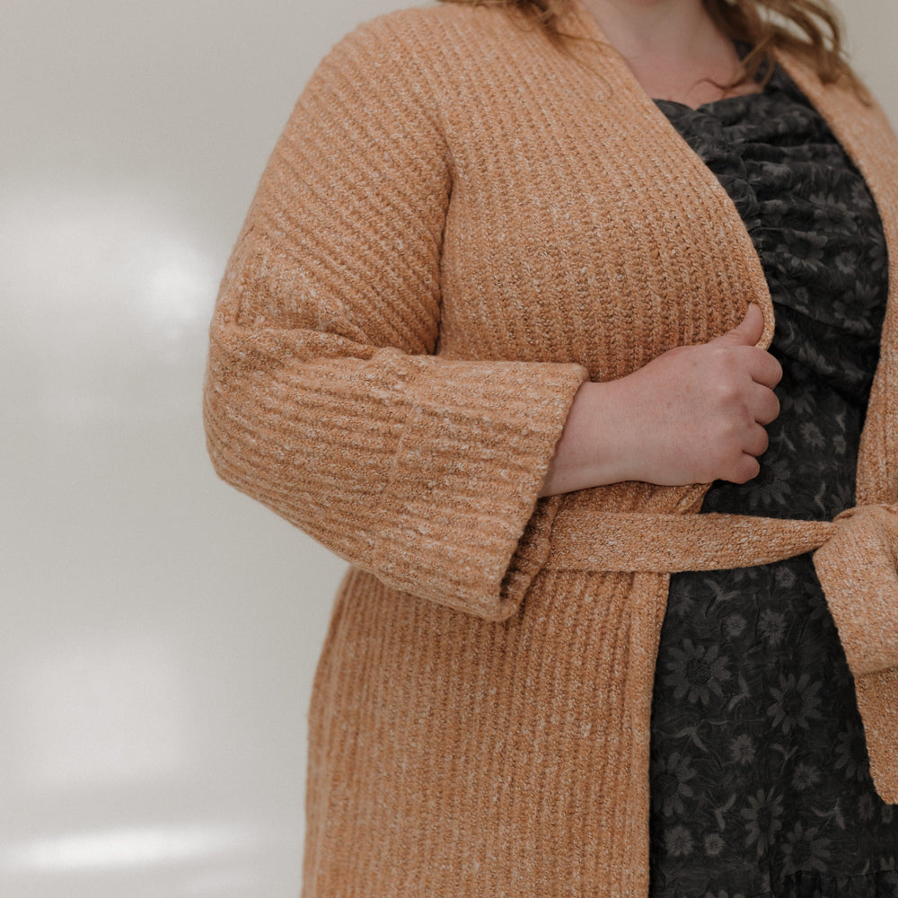 Woman wearing a brown cardigan over a black dress against a neutral background