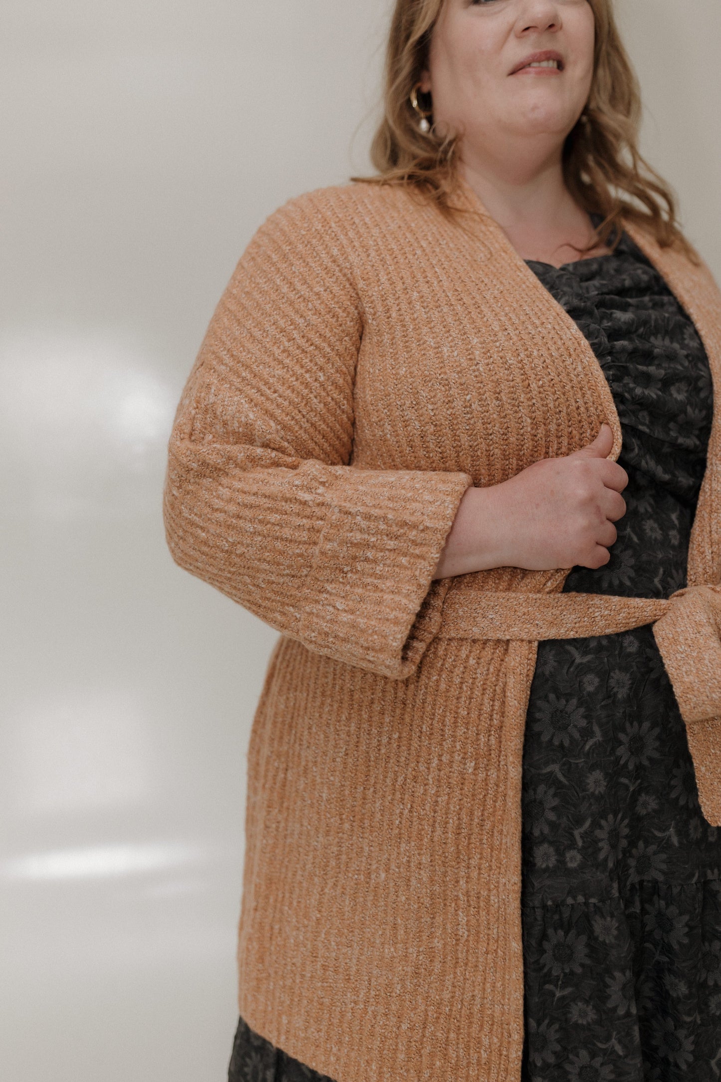 Woman wearing a brown cardigan over a black dress against a neutral background