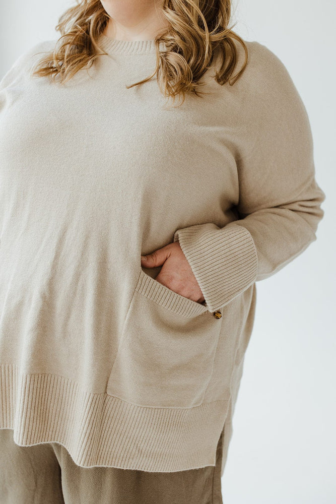 A person wearing the Yesta CUFFED SWEATER WITH POCKETS in a plus size, featuring a ribbed crew neckline and hands tucked into the pockets. Their hair flows freely as they pair this timeless piece with matching pants against a neutral background.