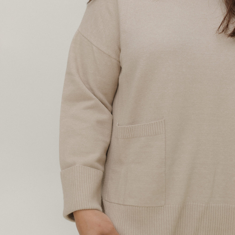 Beige sweater worn by a person on a plain background