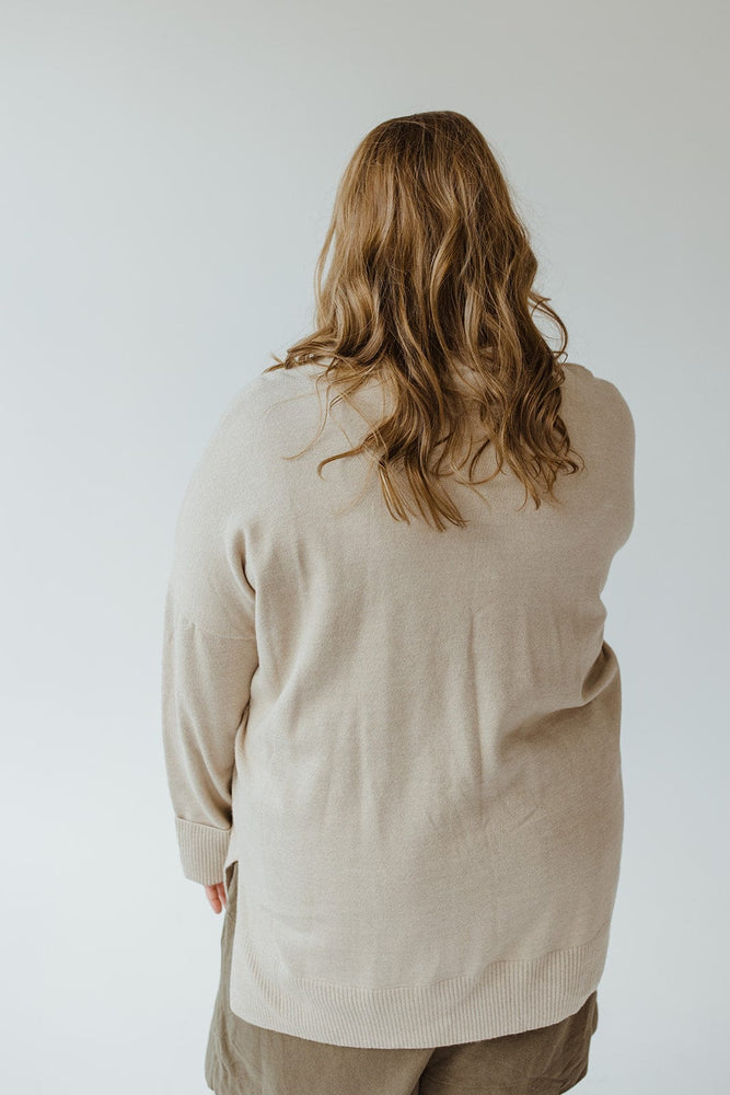 A person with long hair is wearing a luxurious beige Yesta CUFFED SWEATER WITH POCKETS, which features a ribbed crew neckline, and is facing away against a neutral background.