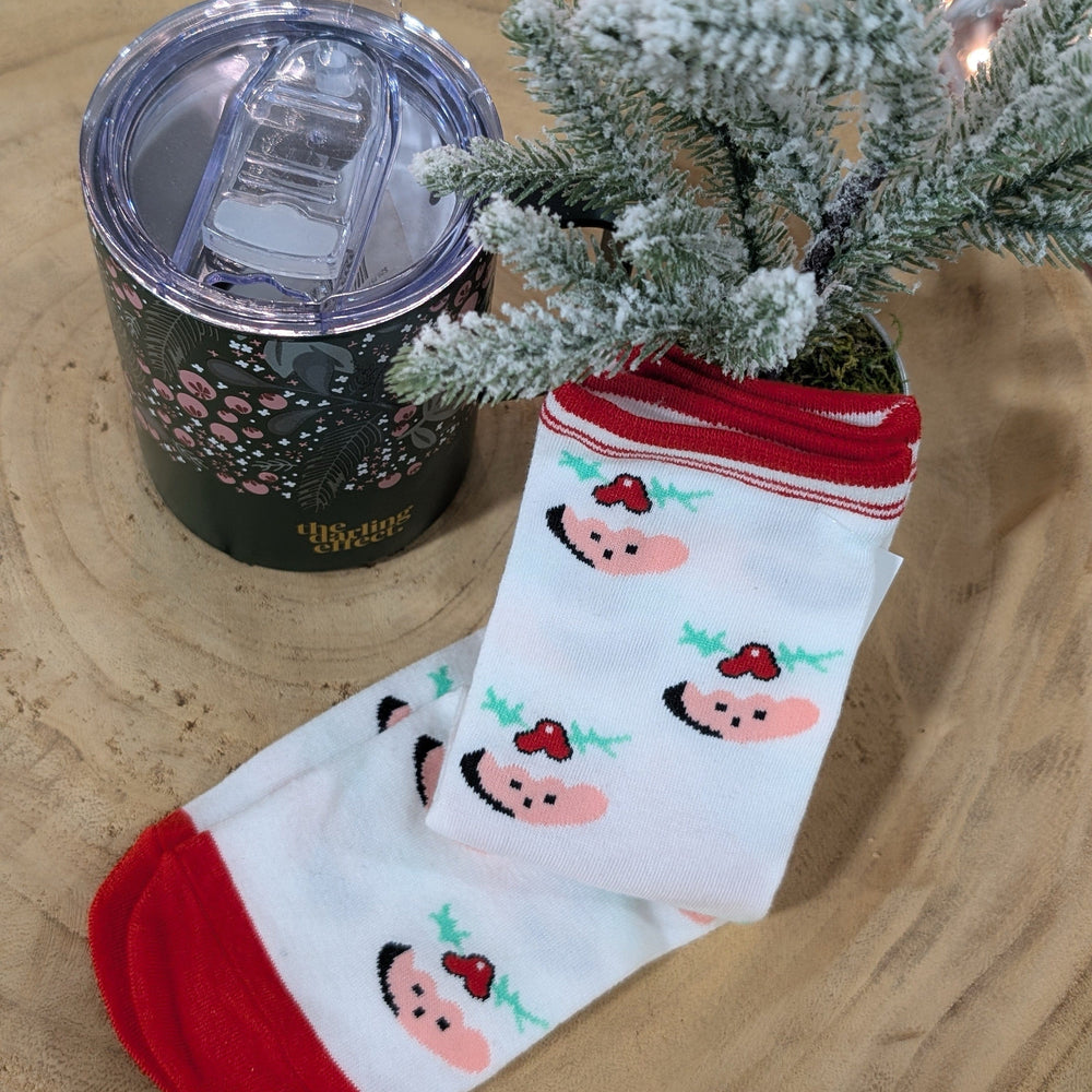 A tumbler, decorated with a floral design, sits beside cozy stylish socks with peach and cherry motifs, displayed near a small frosted pine tree on a wooden surface.