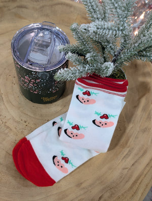 A tumbler, decorated with a floral design, sits beside cozy stylish socks with peach and cherry motifs, displayed near a small frosted pine tree on a wooden surface.