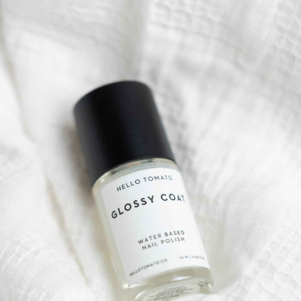 Bottle of 'Glossy Coat' nail polish by Hello Tomato on a white textured background