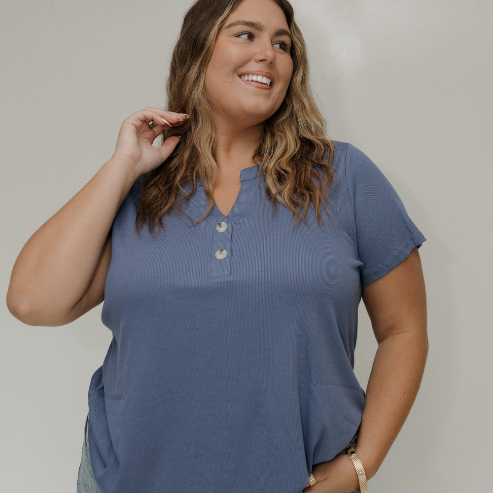 Woman wearing a blue shirt and gray pants against a white wall