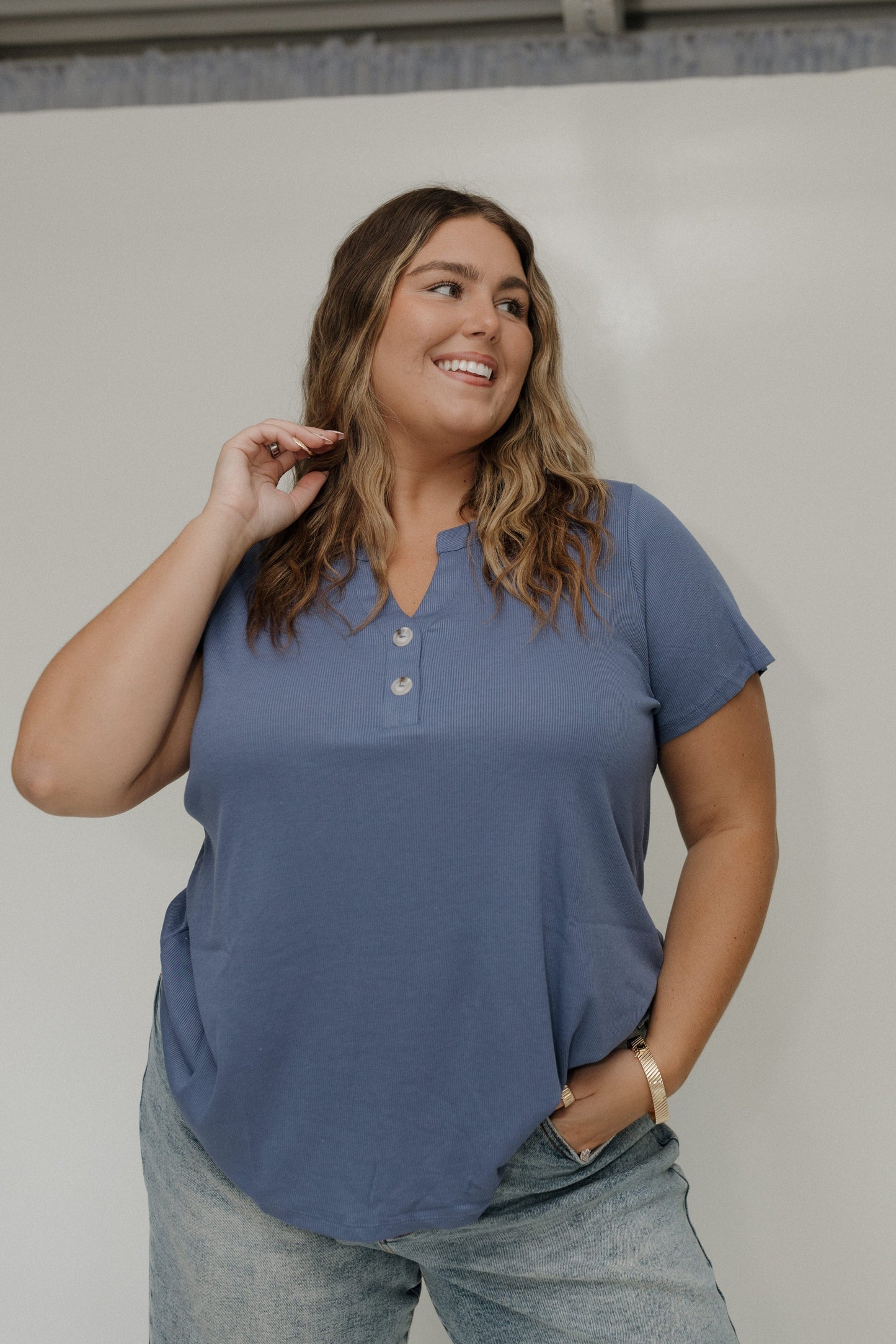 Woman wearing a blue shirt and gray pants against a white wall