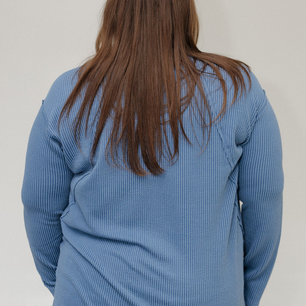 Person wearing a blue textured tee from behind on a plain background