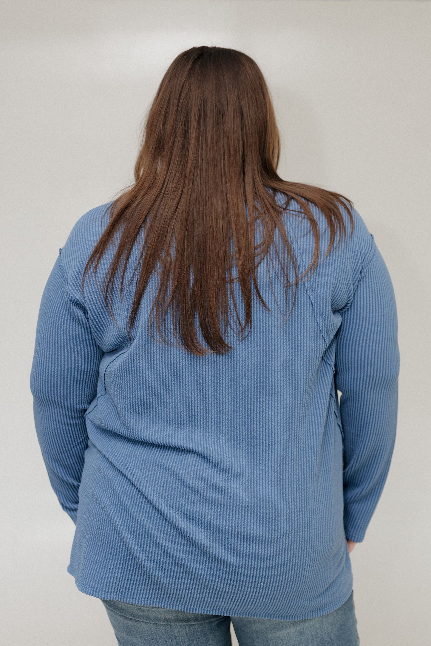 Person wearing a blue textured tee from behind on a plain background